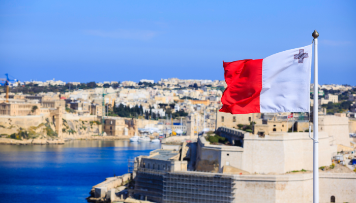Maltesische Flagge vor der Skyline von Valletta mit Festungsmauern und Hafen